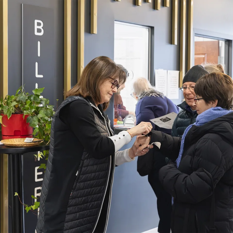 Dame traitant des billets de spectacles de deux visiteurs devant une billetterie