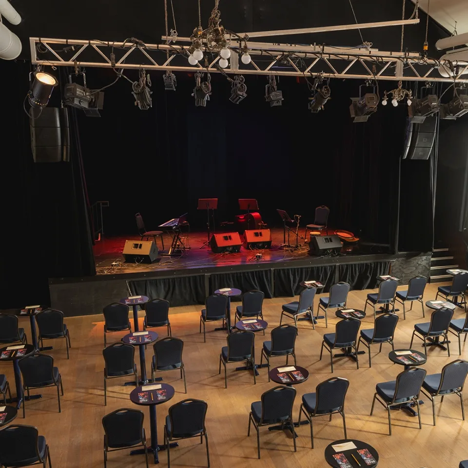 Scène, chaises et tables placées dans la salle Desjardins du Pavillon des arts et de la culture de Coaticook