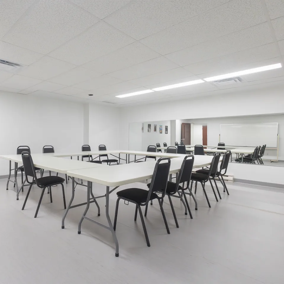 Salle de conférence avec un large miroir et des tables et chaises positionnées en carré.